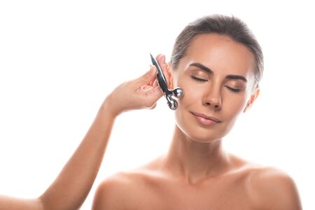naked young woman using facial massager isolated on whiteの写真素材
