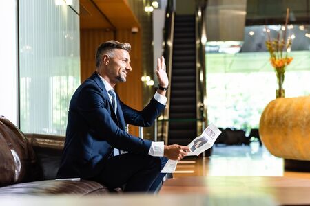 side view of handsome businessman in suit waving and holding newspaperの写真素材
