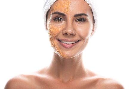 front view of smiling young woman in cosmetic hair band with scrub on face isolated on white