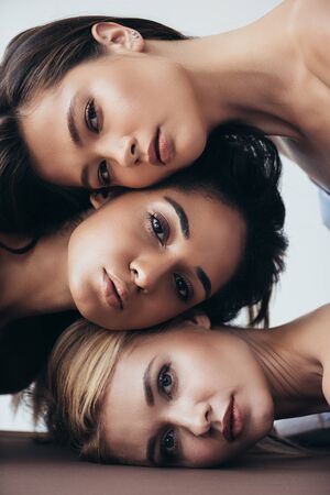 three attractive multiethnic young women looking at camera isolated on greyの写真素材