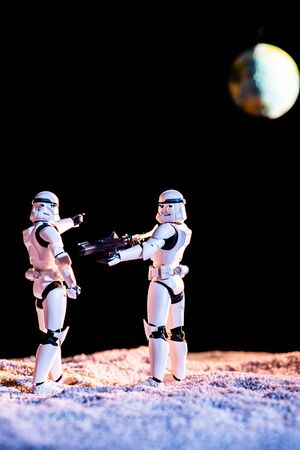 KYIV, UKRAINE - MAY 25, 2019: white imperial stormtrooper aiming with gun at another on black background with planet Earthのeditorial素材