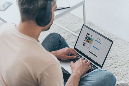 KYIV, UKRAINE - MAY 5, 2019: Man in headphones sitting on floor and using laptop with Instagram app on screen.のeditorial素材