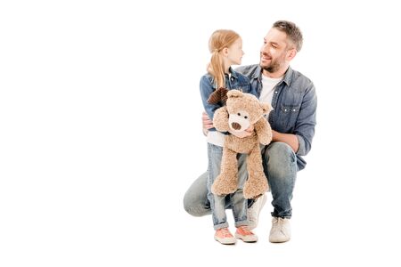 smiling dad and daughter with teddy bear looking at each other isolated on white