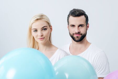 man and beautiful girl with balloons looking at camera isolated on grey