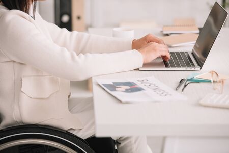 cropped view of disabled businesswoman typing on laptop while sitting at workplaceの写真素材