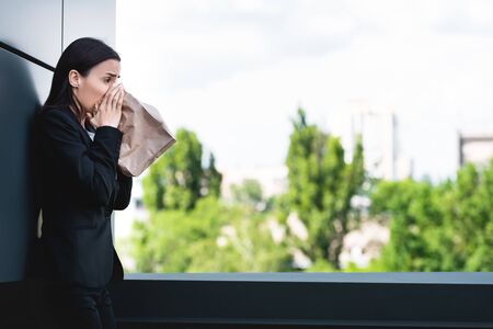 young businesswoman standing on rooftop and breathing into paper bag while suffering from panic attackの写真素材