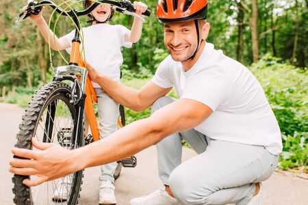 cropped view of son standing and holding handles of bicycle while father checking wheelの写真素材