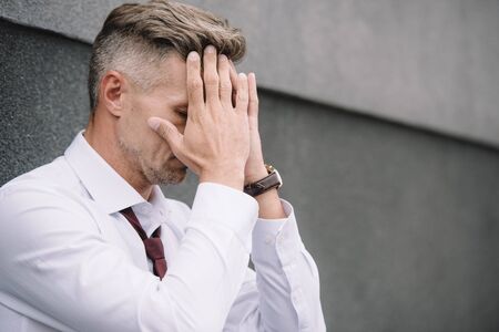 upset businessman in suit covering face with hands