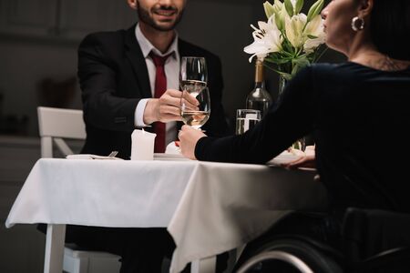cropped view of disabled young woman clinking glasses of red wine smiling boyfriend during romantic dinnerの写真素材