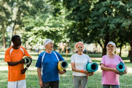 happy retired and multicultural pensioners holding fitness mats in parkの写真素材