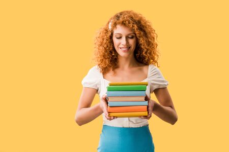 beautiful redhead student holding books isolated on yellowの写真素材