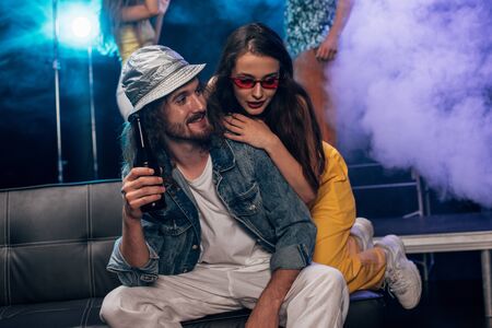 man with alcohol and beautiful girl sitting on couch in nightclubの写真素材