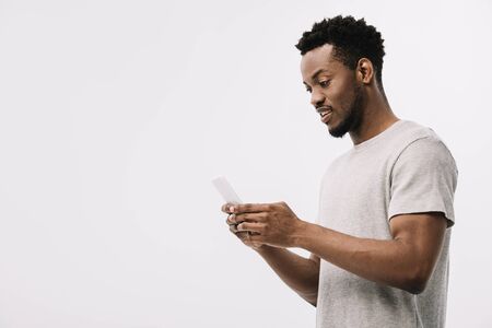 handsome african american man looking at smartphone isolated on whiteの写真素材