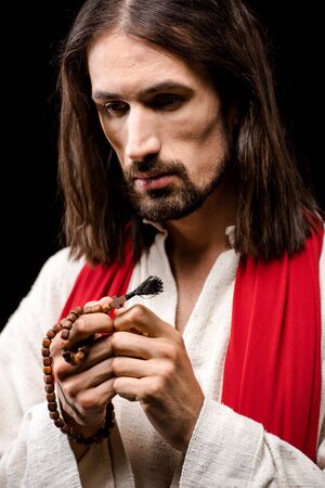 man looking at rosary beads isolated on blackの写真素材