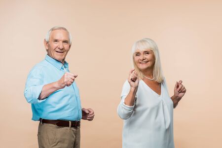 cheerful senior couple gesturing while smiling on beige