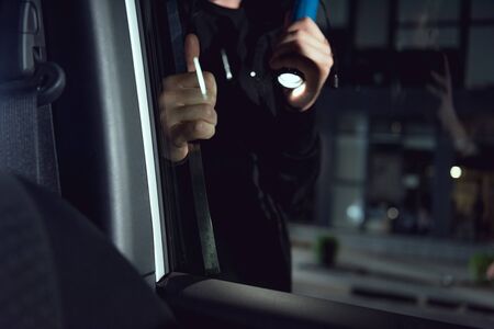 partial view of thief intruding car with flashlight and crowbar
