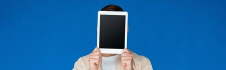 panoramic shot of young man holding digital tablet with blank screen isolated on blueの写真素材