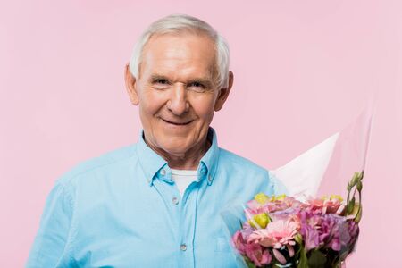 cheerful senior man holding bouquet with flowers isolated on pinkの写真素材