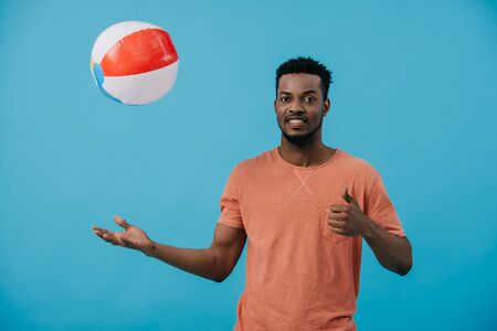 cheerful african american man throwing beach ball in air isolated on blueの写真素材