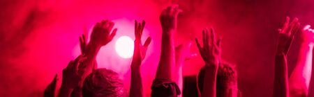 panoramic shot of back view of people with raised hands during rave party in nightclub