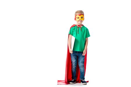 full length view of preschooler kid in mask and hero cloak holding digital tablet on whiteの写真素材