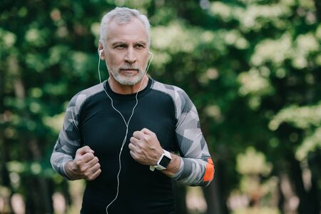 handsome mature sportsman listening music in earphones while running in parkの写真素材