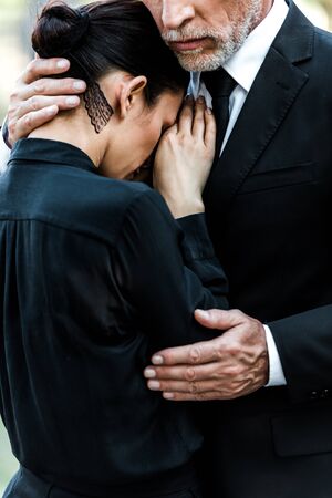 cropped view of upset senior man hugging woman on funeralの写真素材