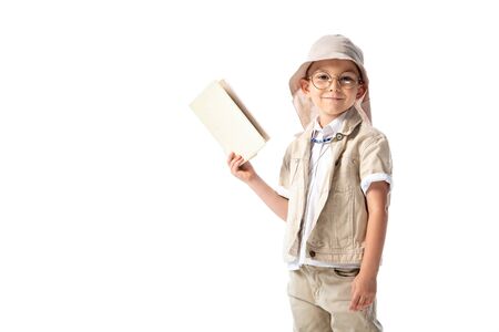 smiling explorer child in glasses holding book and looking at camera isolated on whiteの写真素材