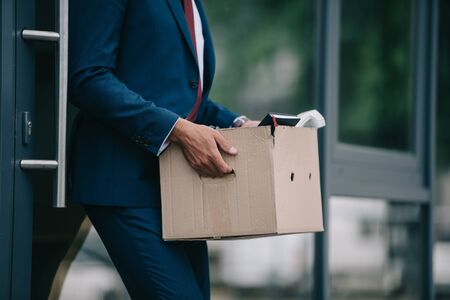 cropped view of fired businessman standing near building and holding carton boxの写真素材