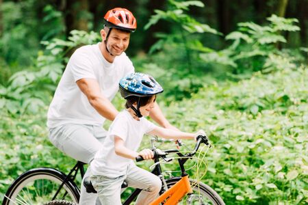 father and son riding bicycles while dad looking at kidの写真素材