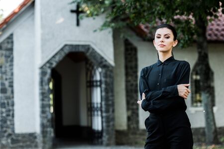 attractive woman standing with crossed arms near churchの写真素材