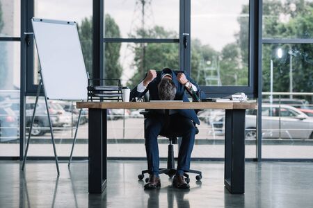 businessman sitting near desk with clenched hands in modern officeの写真素材