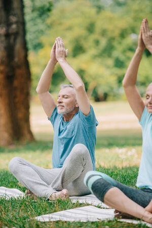 mature man and woman meditating in lotus poses with closed eyes in parkの写真素材