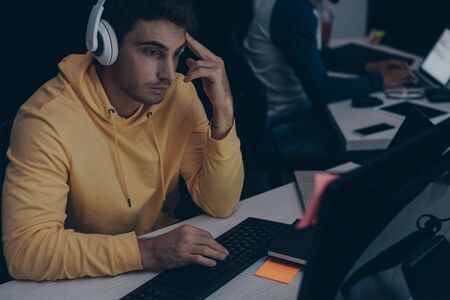 selective focus of young programmer in headphones working on computer near african american...