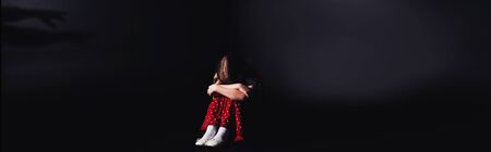 panoramic shot of depressed child sitting with bowed head on black backgroundの写真素材