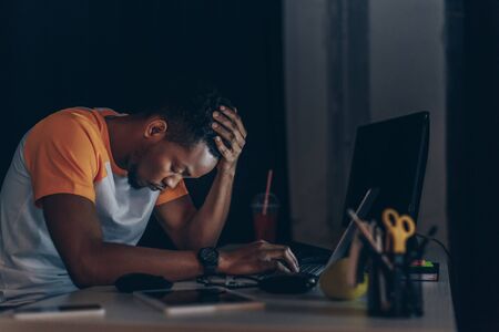sleepy african american programmer sitting at workplace with closed eyesの写真素材