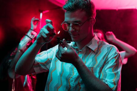 man lighting smoking pipe with marijuana in nightclub