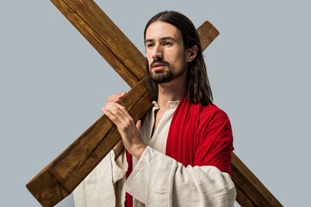 handsome bearded man in jesus robe holding wooden cross isolated on greyの写真素材