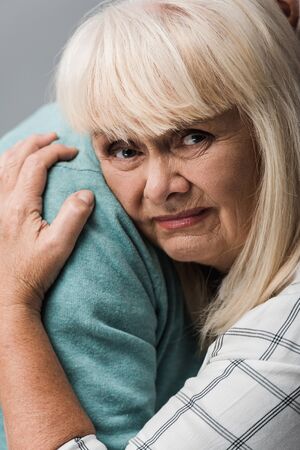 close up of husband hugging sad retired wife with grey hair isolated on greyの写真素材