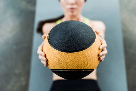 selective focus of woman holding ball while lying on fitness matの写真素材