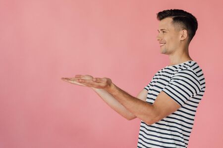smiling man in striped t-shirt pointing with hands isolated on pinkの写真素材