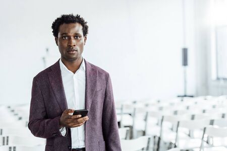 african american businessman in formal wear holding smartphone in conference hallの写真素材