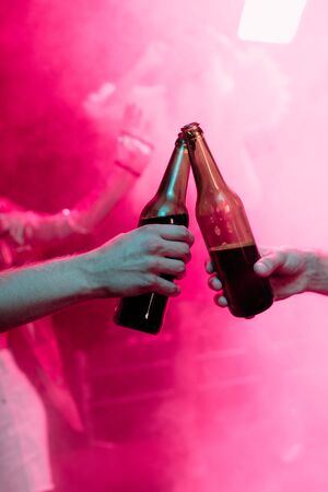 cropped view of men clinking with beer bottles in nightclubの写真素材