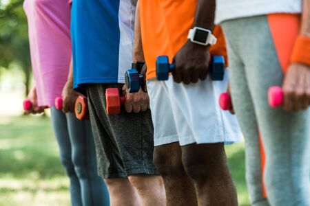 cropped view of multicultural pensioners in sportswear holding dumbbells in parkの写真素材