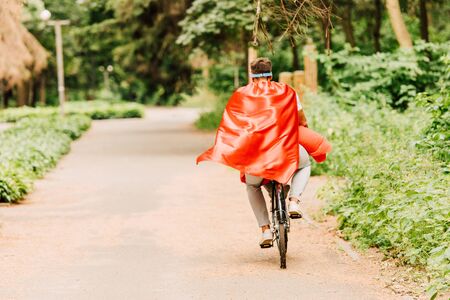 back view of father and son riding bicycle in red cloaksの写真素材