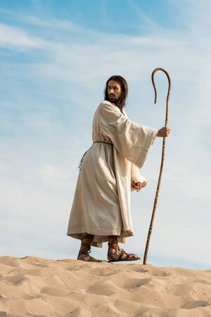 bearded man walking with wooden cane in desertの写真素材