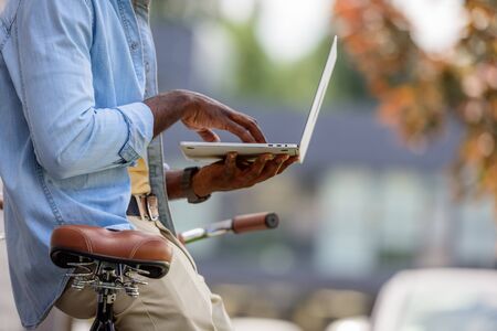 cropped view of african american man using laptop while standing near bicycle