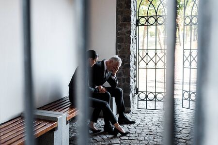 beautiful woman sitting on bench near sad senior man in cemeteryの写真素材