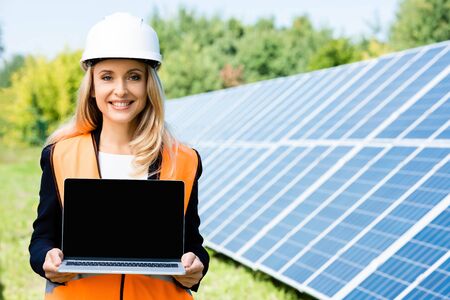 attractive businesswoman in hardhat and safety vest holding laptop with copy space