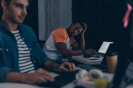 selective focus of african american programmer looking at multicultural colleague while working...